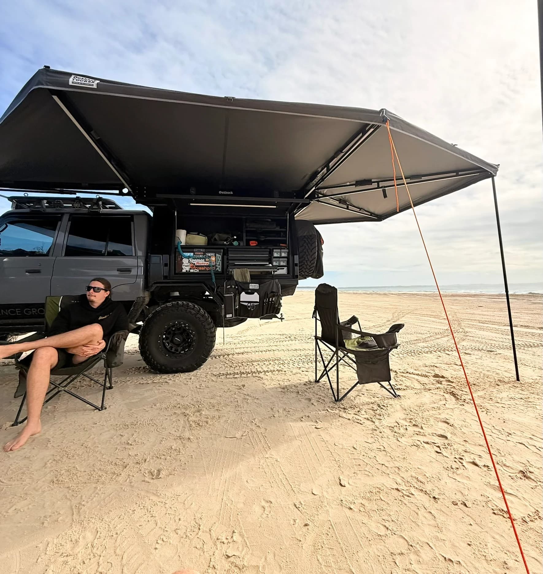 The canopy open under the awning on the beach, camp chairs set out.
