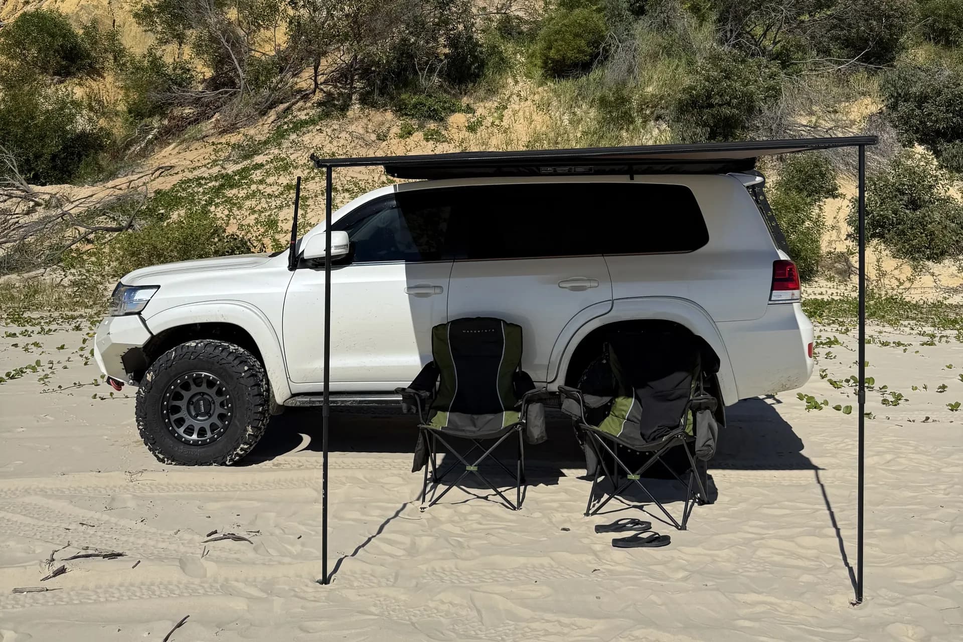 A 200 Series on the sand with an awning out over two camp chairs.