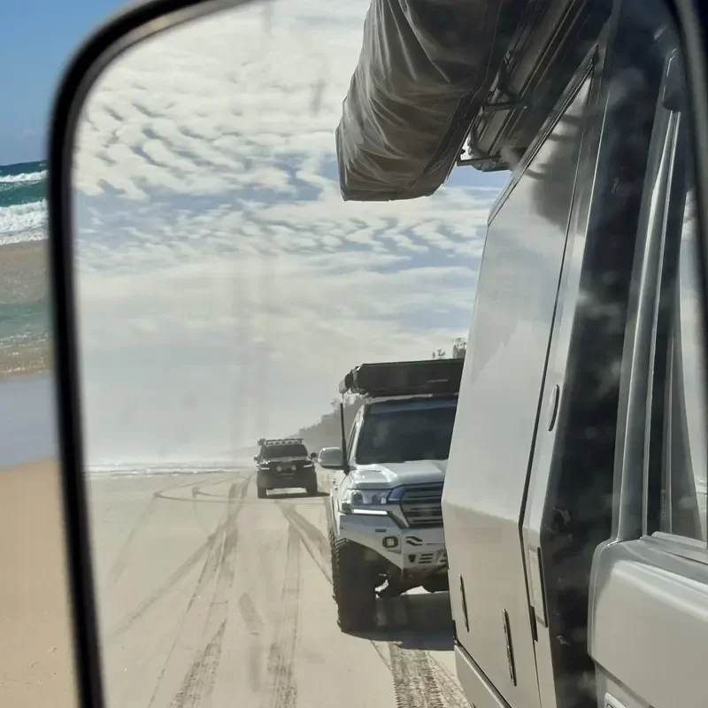 A 4x4 following along the beach, seen in the side mirror.